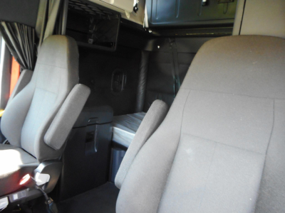 Cab interior of a Freightliner Cascadia 126 sleeper truck showing front seats and sleeper area with overhead storage.