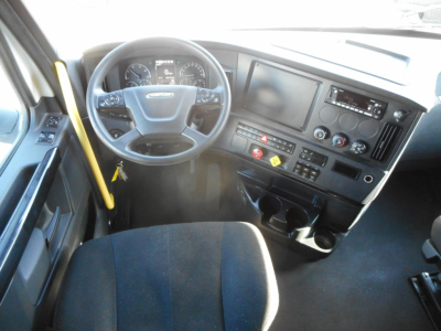 Freightliner Cascadia 126 truck cockpit interior showing steering wheel, dashboard, digital gauges, center console, and gear shifter with cup holders.