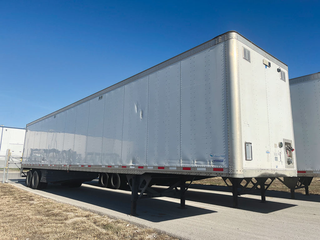 Vanguard aluminum cargo trailer viewed from side and rear, with smooth riveted aluminum walls and tandem axles, under clear blue sky.