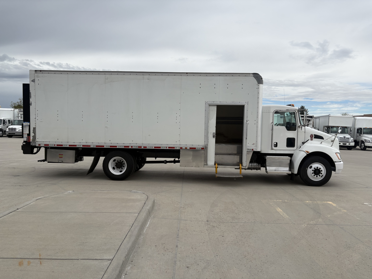 Kenworth T270 box truck side profile showing a white cargo box with a side entry door and steps, and a front cab with black tires.
