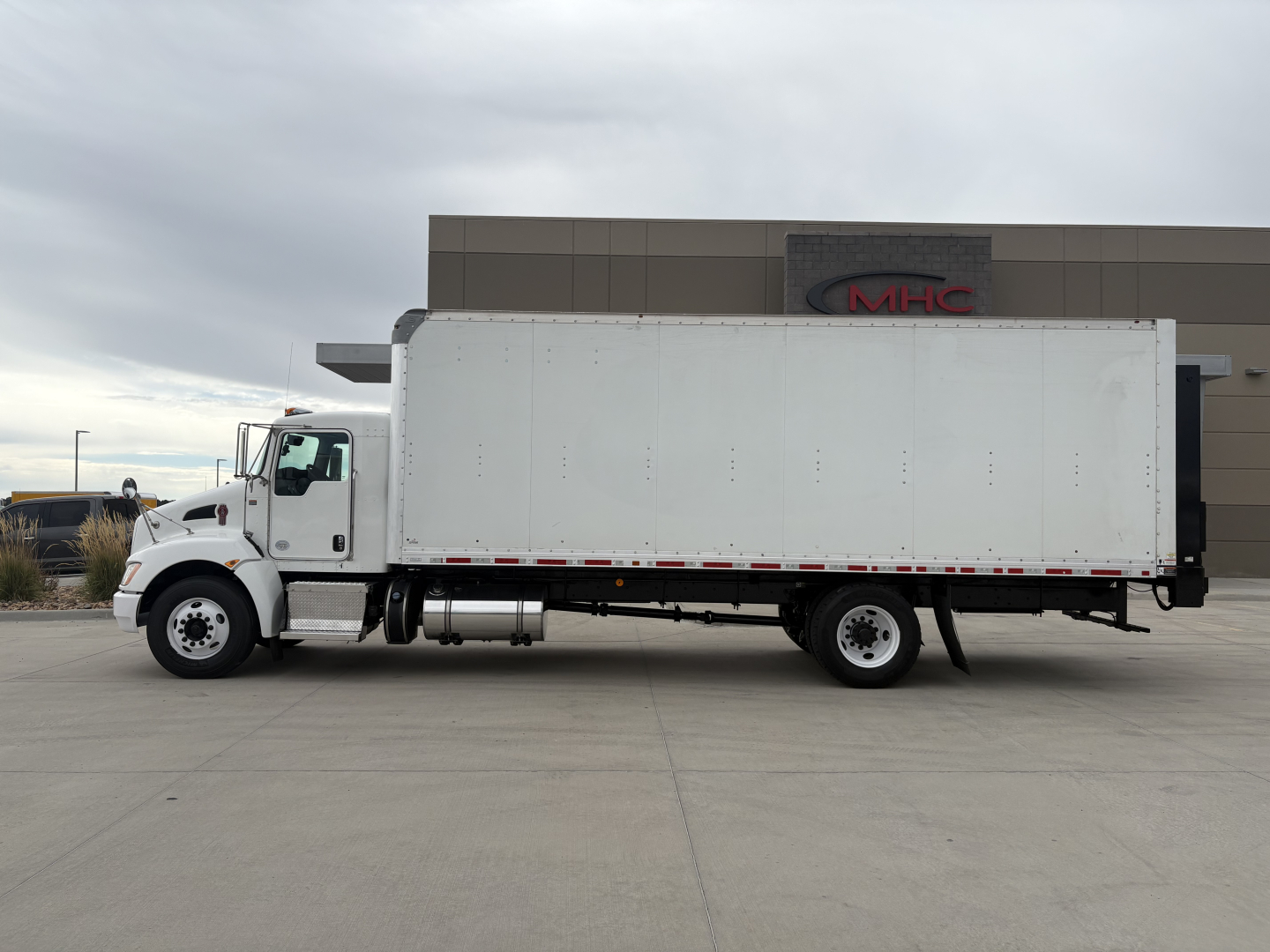Kenworth T270 box truck side view showing white cargo box and cab with black chassis, on a concrete lot. No visible text on vehicle panels.