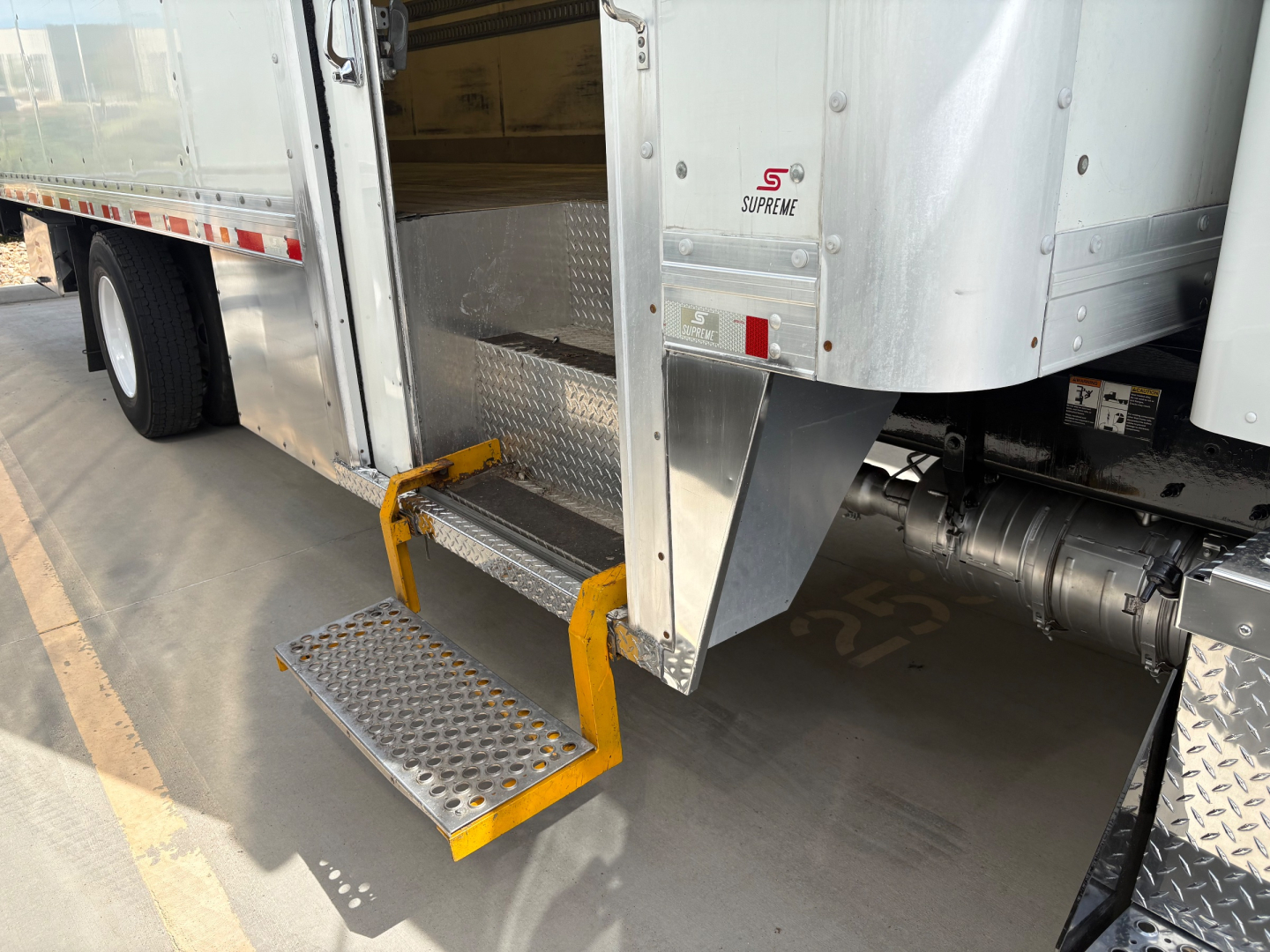 Kenworth T270 box truck with side entry steps extended from cargo area, aluminum diamond plate lowers and yellow steps, visible rear dual tires and undercarriage components.
