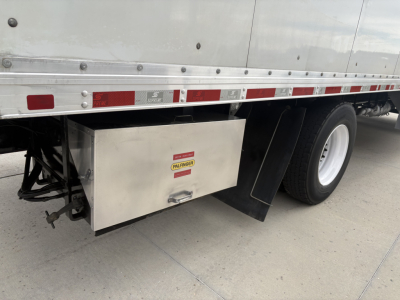 Truck side view showing aluminum toolbox mounted under the cargo bed of a 2020 Kenworth T270 with box body, rear dual wheels, reflective tape, and stock number 0630677.