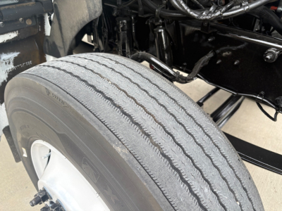 Truck wheel and front suspension of a 2020 Kenworth T270 showing tire tread and wheel well; visible components include frame and undercarriage.