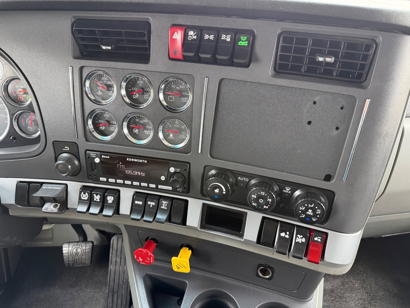 Dashboard of a 2020 Kenworth T680 with multiple gauges, center controls, and red/black toggle switches; visible yellow and red handles below.