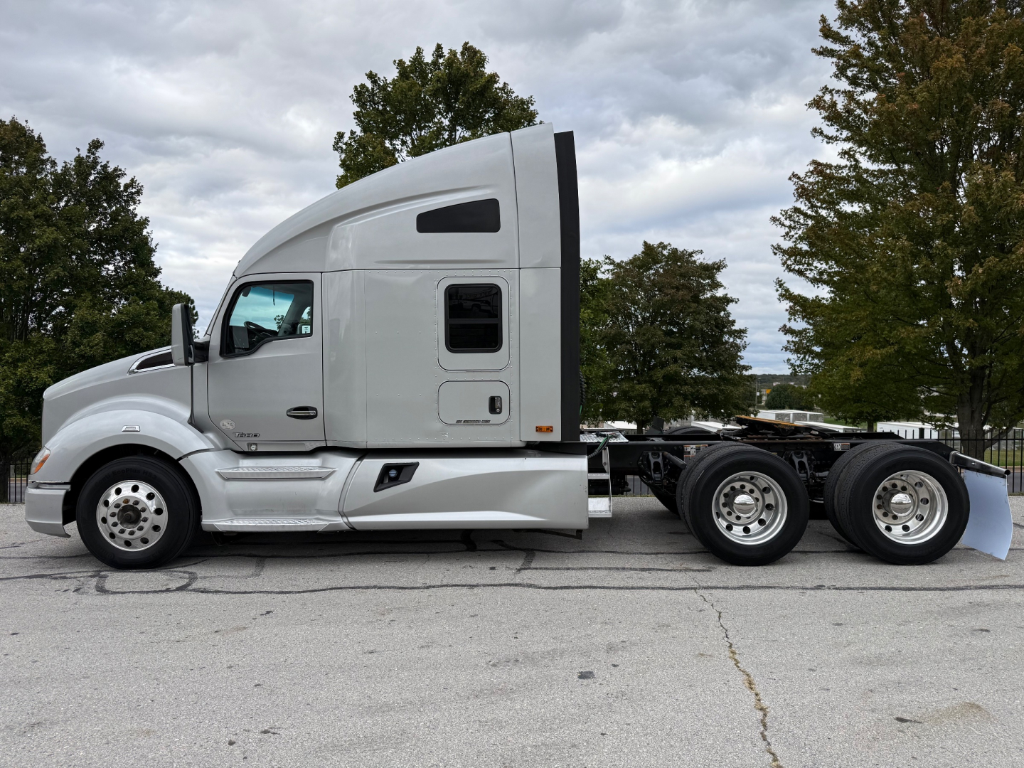 Kenworth T680 tractor side view showing sleeper cab and dual rear axles with chrome wheels and white paint.