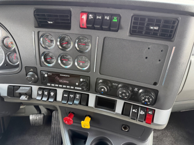 Dashboard of a 2020 Kenworth T680 with multiple gauges, center controls, and red/black toggle switches; visible yellow and red handles below.