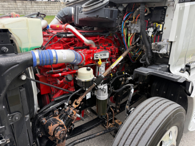 Kenworth T680 engine bay with red engine block, blue intake hose, various wires, coolant reservoir, and filtration components visible.