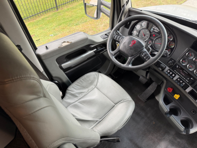 Truck interior showing steering wheel with logo, dashboard gauges, center console, and gray driver seat in a Kenworth T680 cab.