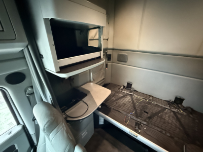 Kenworth truck sleeper cab interior showing side bunk area with open overhead cabinet and sleeping platform.