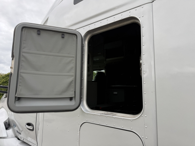 Kenworth T680 truck cab window with door open showing interior; exterior white paint and riveted panel.