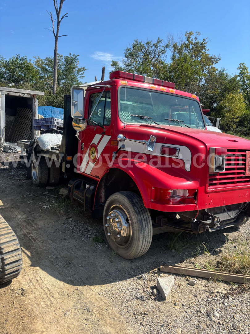 International 4700 low-profile truck showing red cab and flatbed, front-side view.