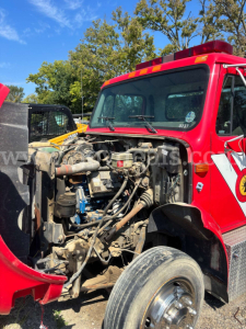 Truck engine bay view of a red 1999 International 4700 with hood open showing engine components and hoses.
