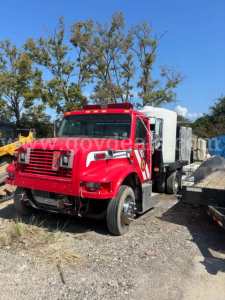 International 4700 low profile truck in red with white cab sleeper, front grille, dual headlights, flatbed with equipment in yard.