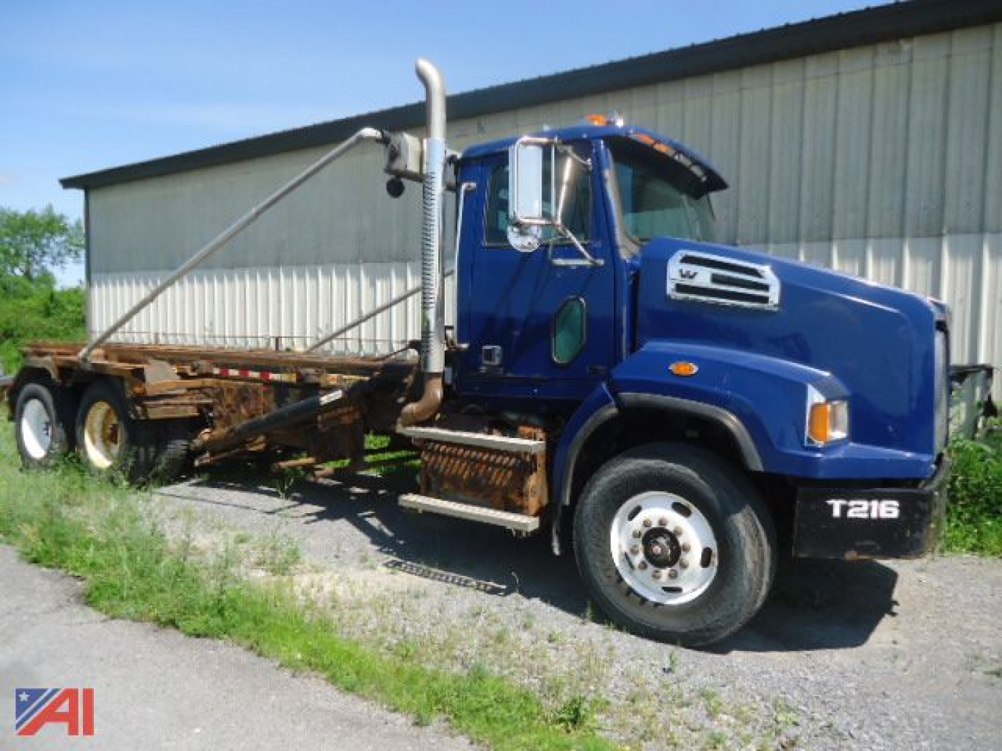 Blue 2015 Western Star 4700 SB roll off truck in side view showing exhaust stack and rear loading mechanism.
