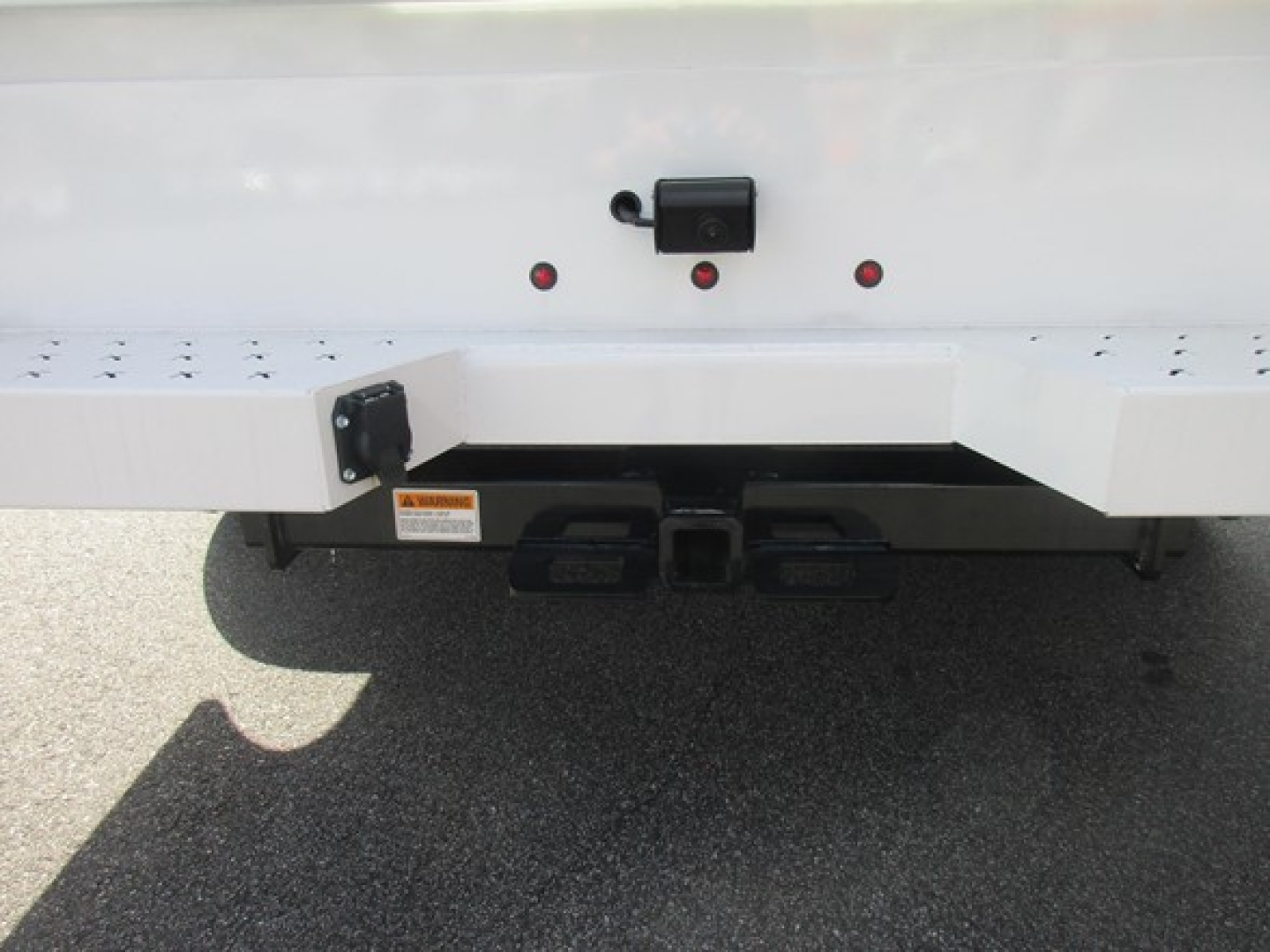 Rear view of a Ford F-350 service/utility truck showing the hitch area and bumper. Visible text includes a small orange warning label and the central hitch plate.