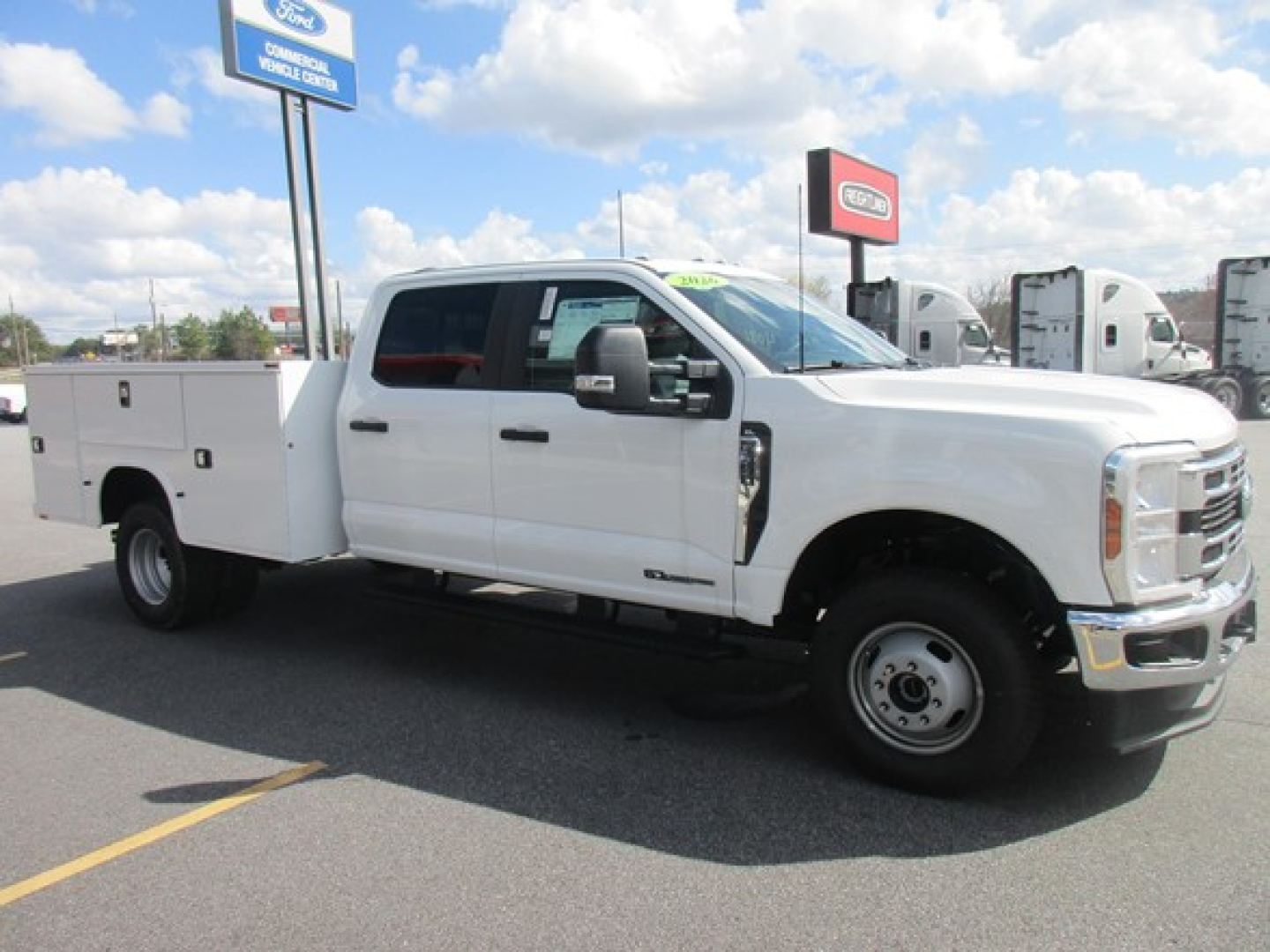 White Ford F-350 service/utility truck with utility bed, side steps, large mirrors, and dual rear wheels visible in a dealership lot.