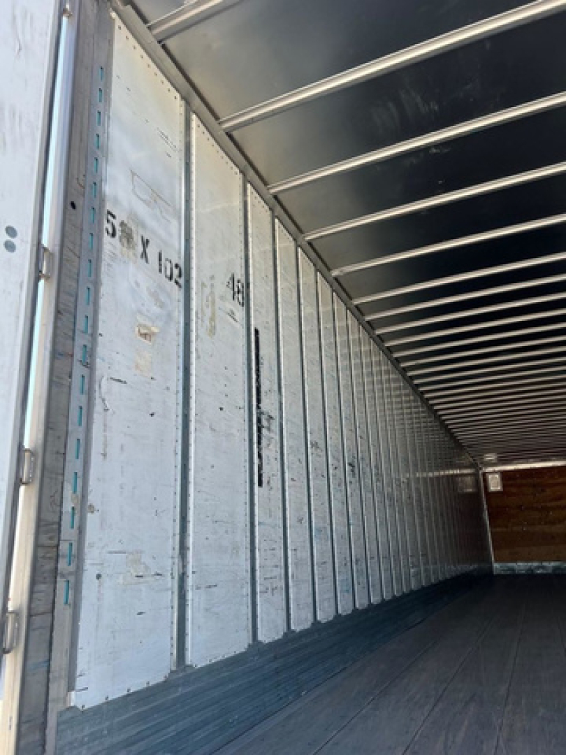 Inside view of a cargo trailer with metallic walls showing vertical measurement marks and door tracks
