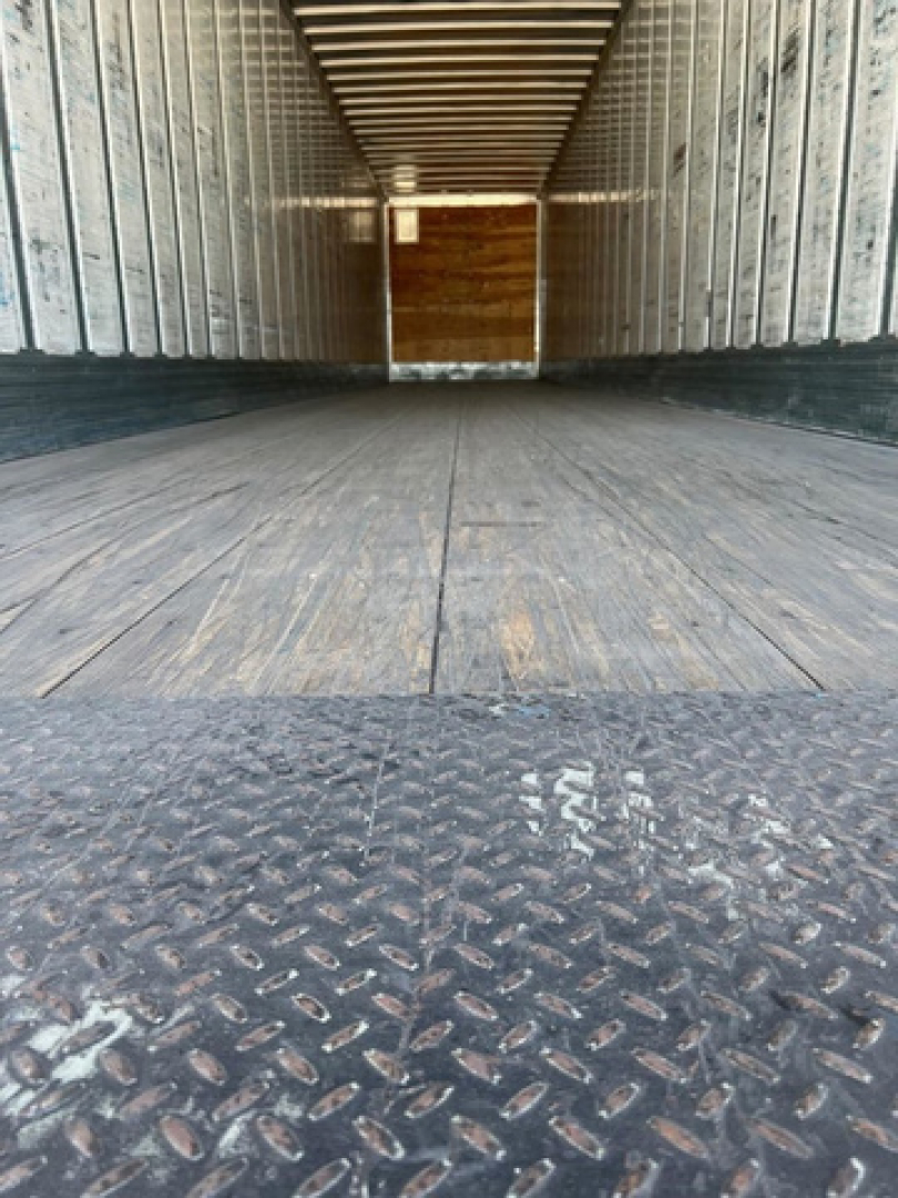 Interior of a empty utility van trailer with metal side walls and a wooden floor, taken from the rear looking forward.