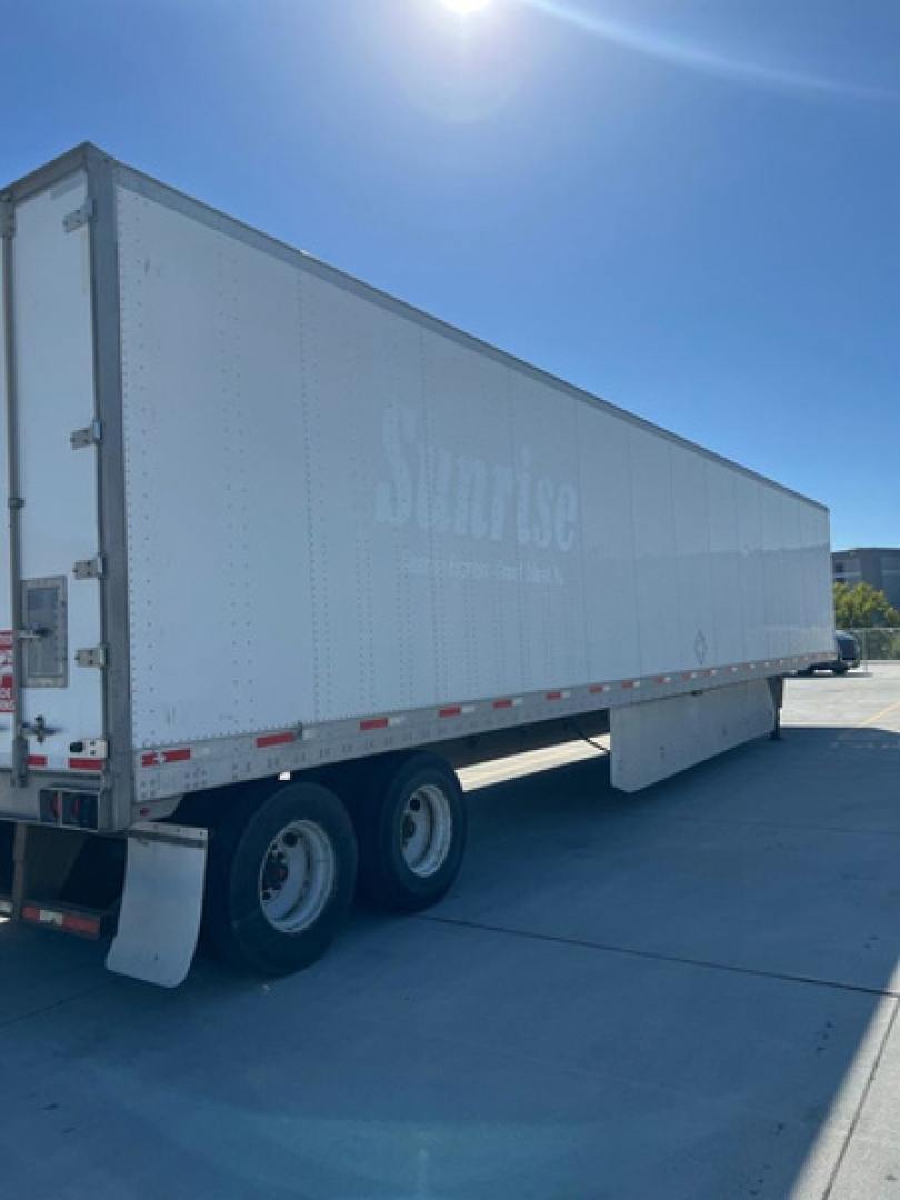 Utility van trailer showing tandem rear wheels and side logo faintly visible on white cargo box