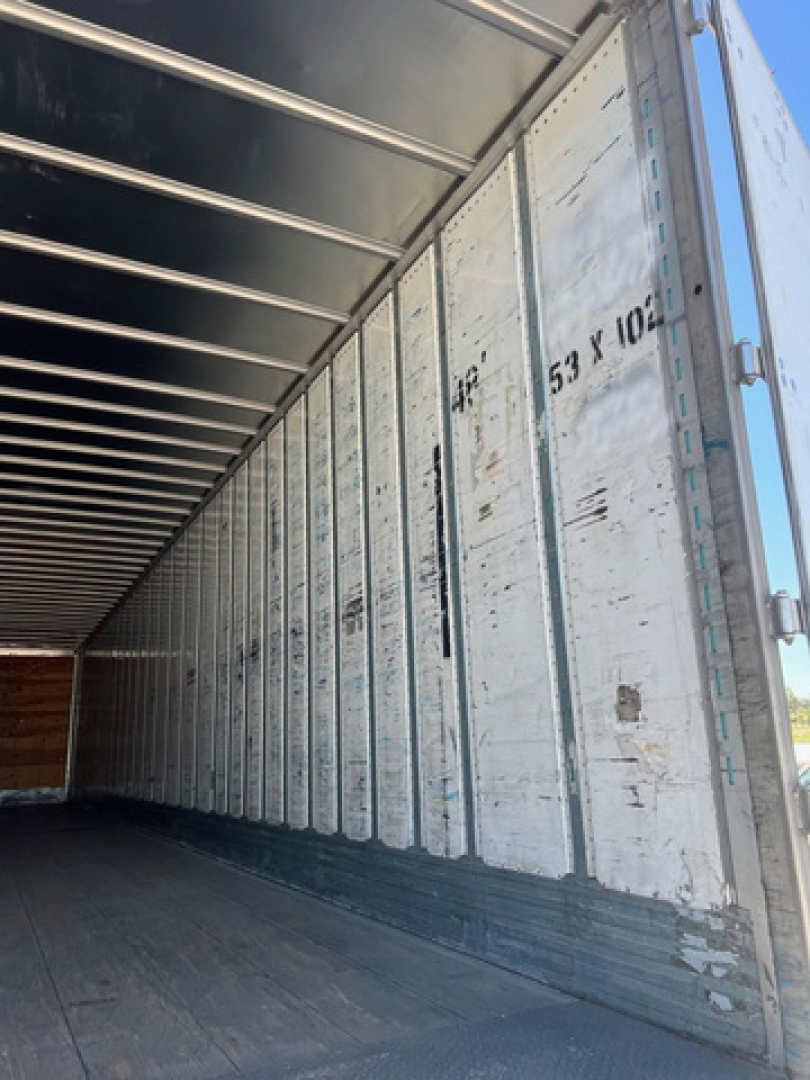 Inside of a utility van trailer showing vertical metal wall panels with stamped numbers and a dark floor.
