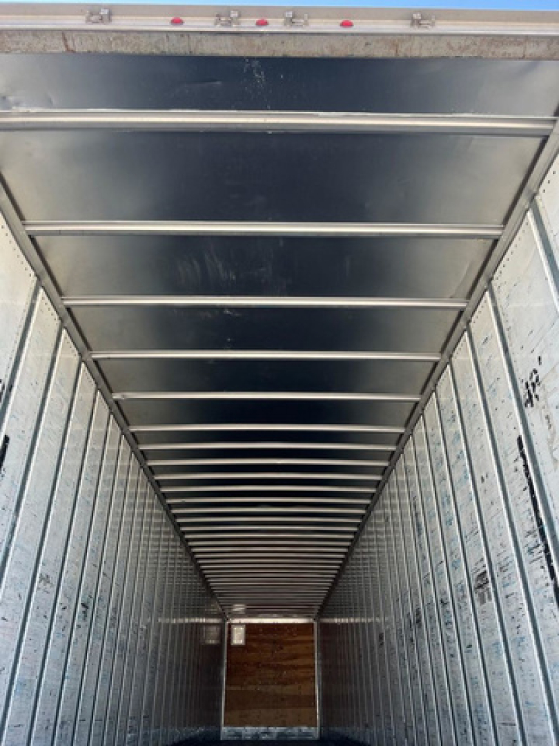 Trailer interior showing metal walls and ceiling ribs, creating a long narrow cargo space with a wooden floor at the far end.