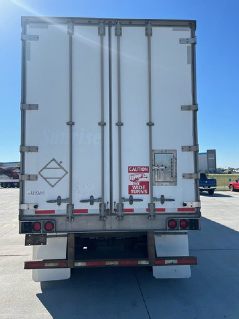 Rear view of a white utility van trailer with double doors, warning sticker, reflectors, and taillights.