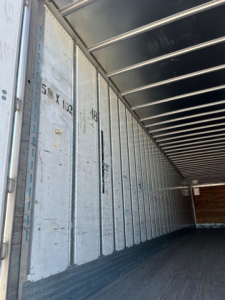 Inside view of a cargo trailer with metallic walls showing vertical measurement marks and door tracks