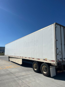 Trailer side view of a 2012 utility van trailer showing riveted metal exterior and dual rear wheels.