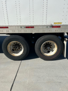 Trailer wheels and side of cargo van/trailer showing dual rear wheels and lower side rail.