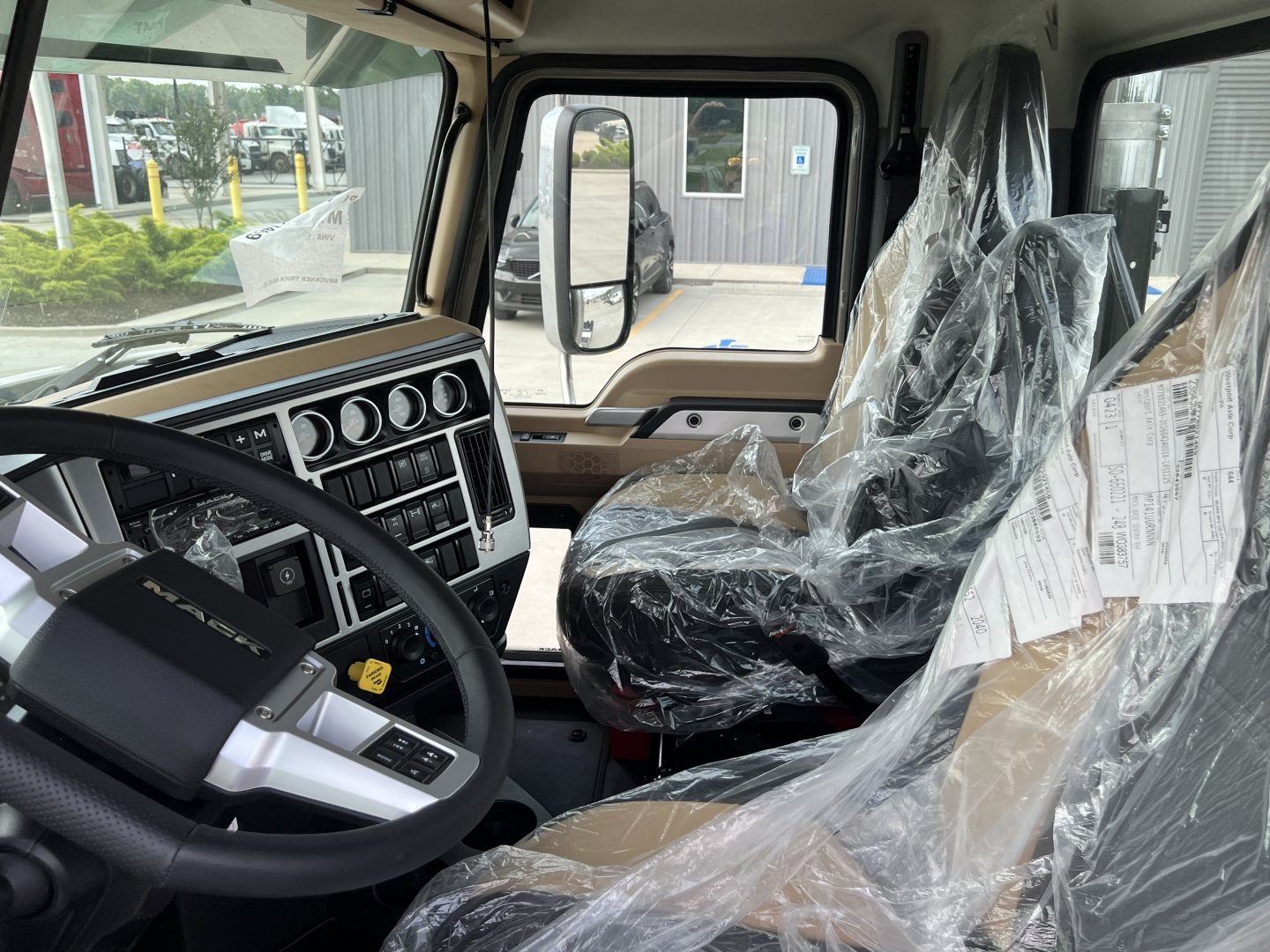 Interior of a new 2027 Mack PI64T Daycab truck showing steering wheel, dashboard gauges, and plastic-covered seats.