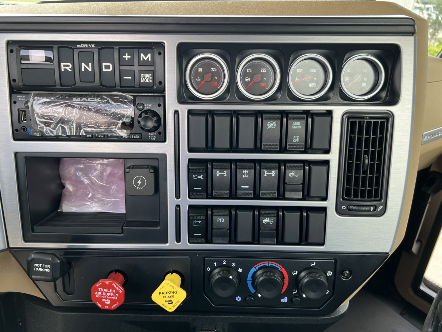 Dashboard and center console of a Mack PI64T truck showing gauges, shifter area, climate controls, and various switches.