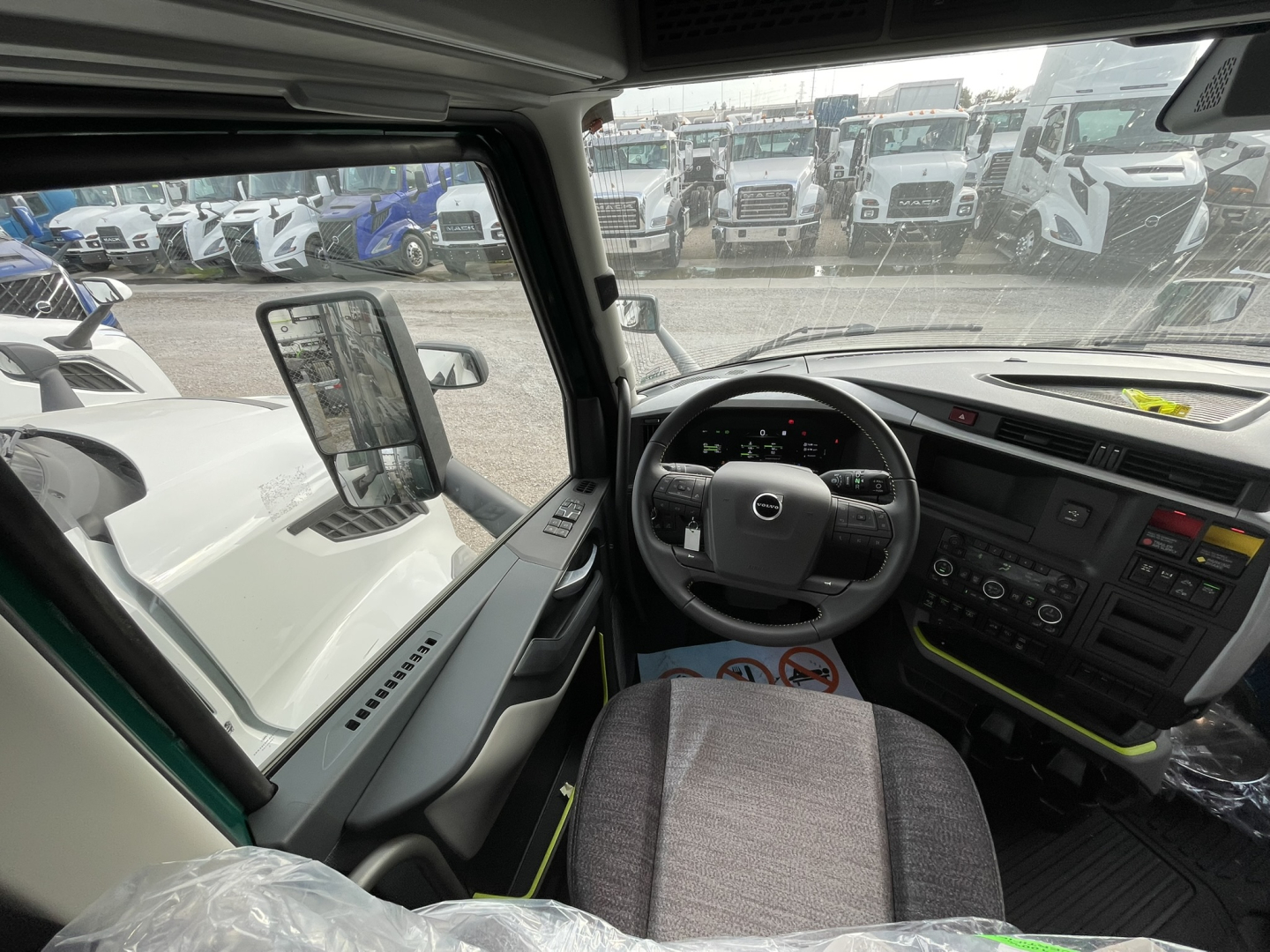 Volvo VNL cab interior view showing steering wheel and dashboard with large central display, driver seat, and side window.