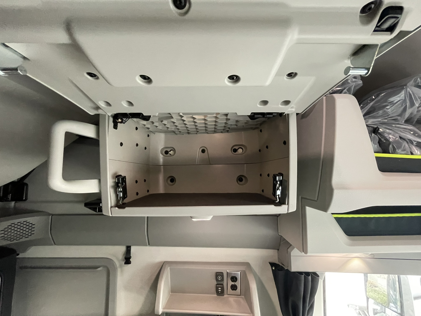 Open center console/storage compartment in Volvo VNL64T860 cab showing empty tray with metal latches and surrounding dashboard panels.
