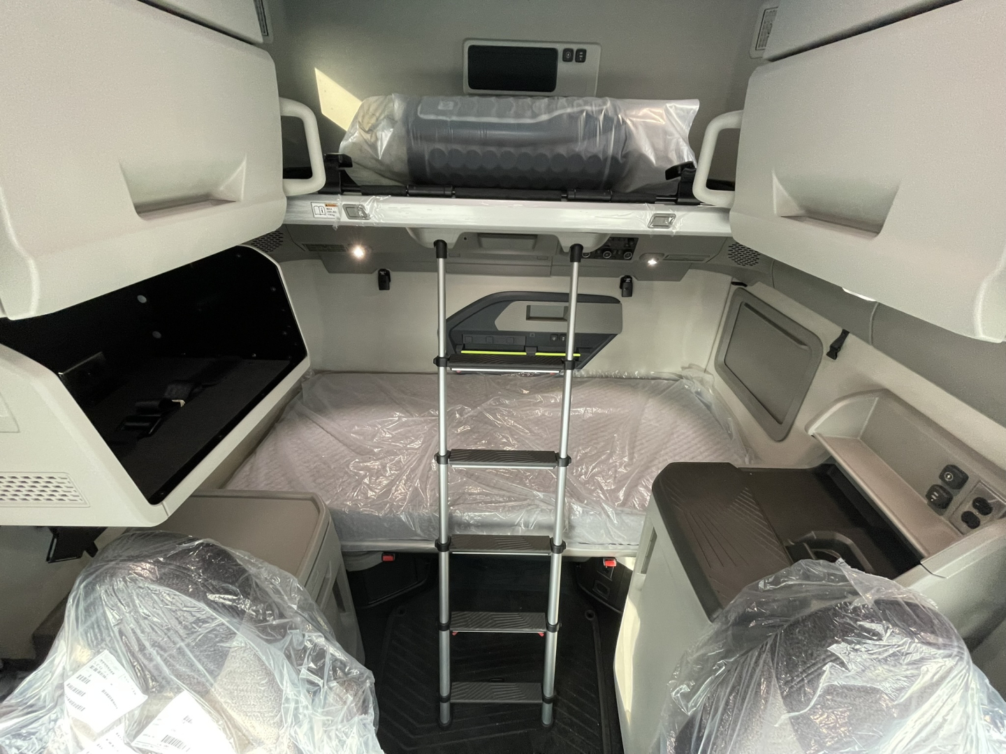 Volvo VNL64T860 sleeper cab interior showing upper bunk, ladder, and plastic-wrapped seating areas.