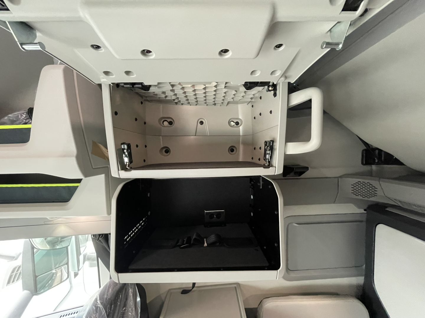 Interior storage compartments of a Volvo VNL truck cab with open overhead compartments and a dark lower storage bay.