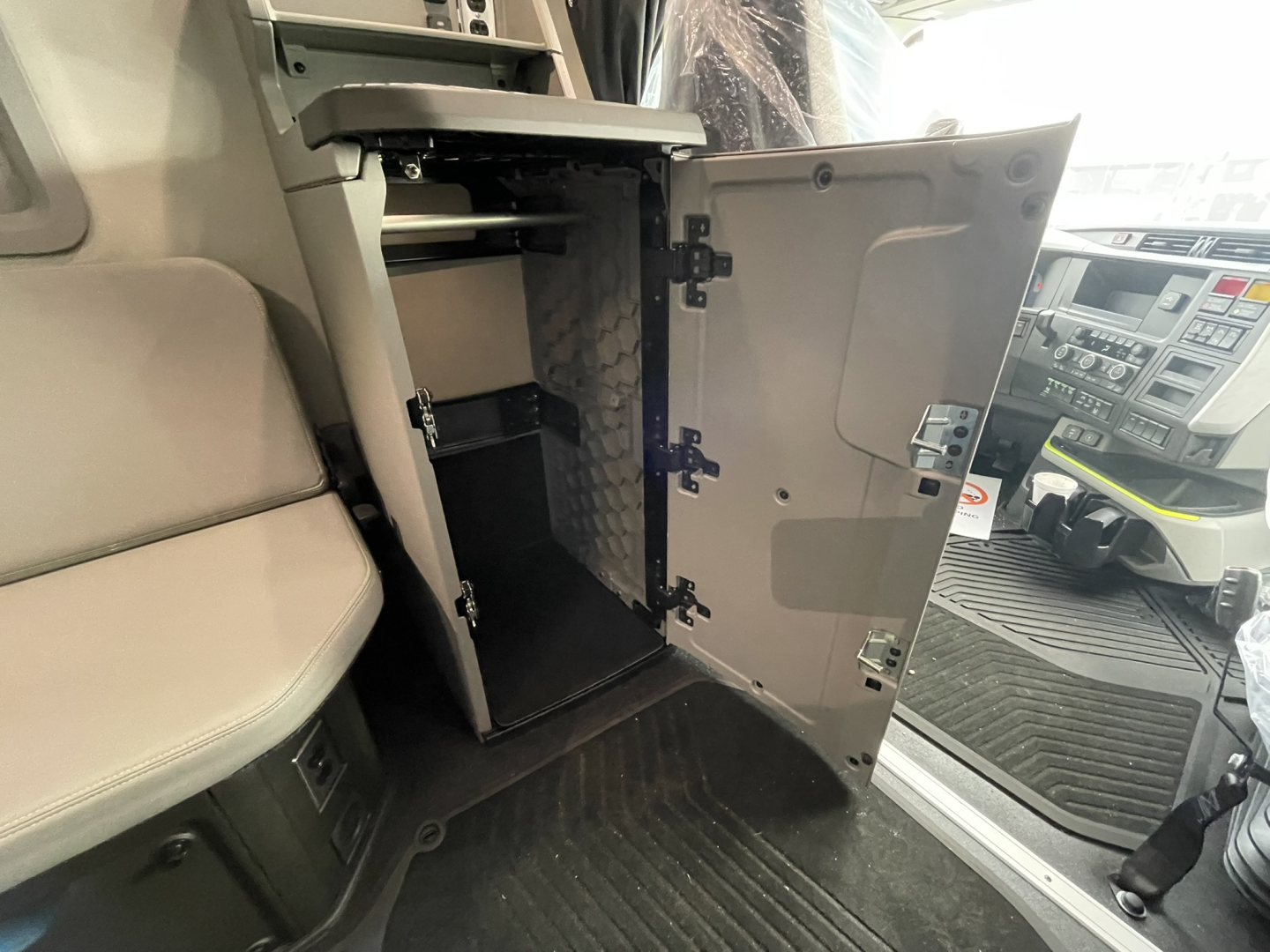 Truck interior with open cabinet/locker in the cab area, showing multiple storage compartments and a small vertical shelf inside a cabinet near the driver seat.