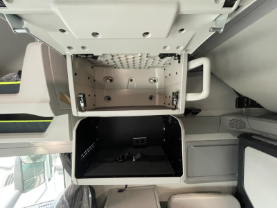 Interior storage compartments of a Volvo VNL truck cab with open overhead compartments and a dark lower storage bay.