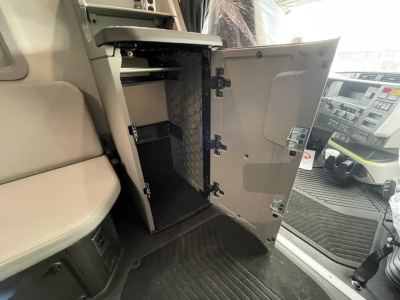 Truck interior with open cabinet/locker in the cab area, showing multiple storage compartments and a small vertical shelf inside a cabinet near the driver seat.
