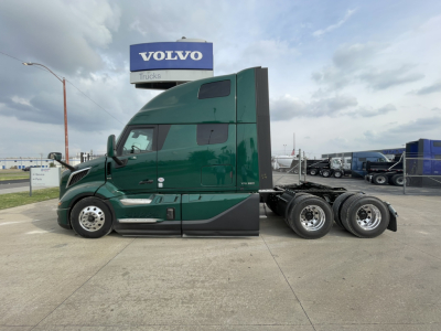 Volvo VNL64T860 sleeper tractor side view showing green cab and dual rear axles, inventory lot background with Volvo sign.