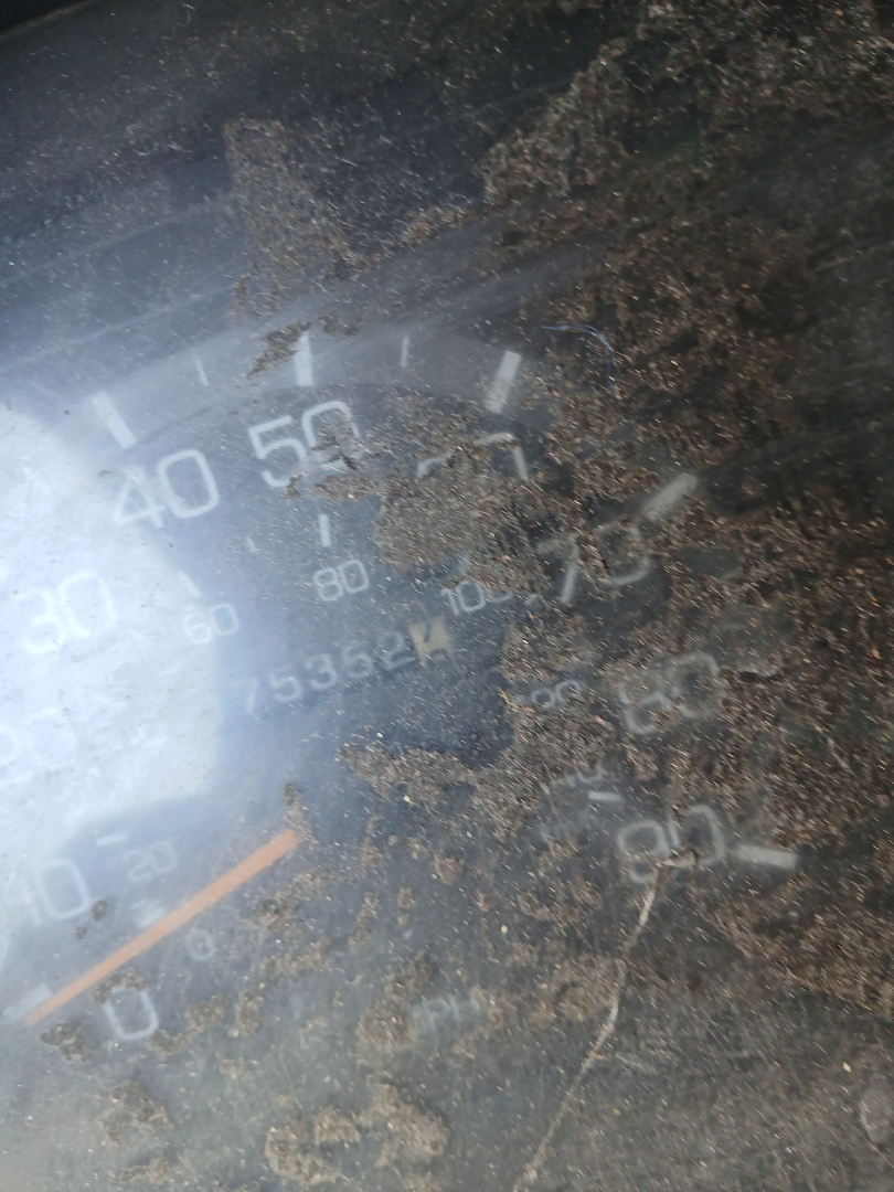 Gauge cluster close-up showing speedometer with numbers and a sediment of dirt; markings include 0-50-60 and 100, with a needle near 0; dirt obscures surrounding text.