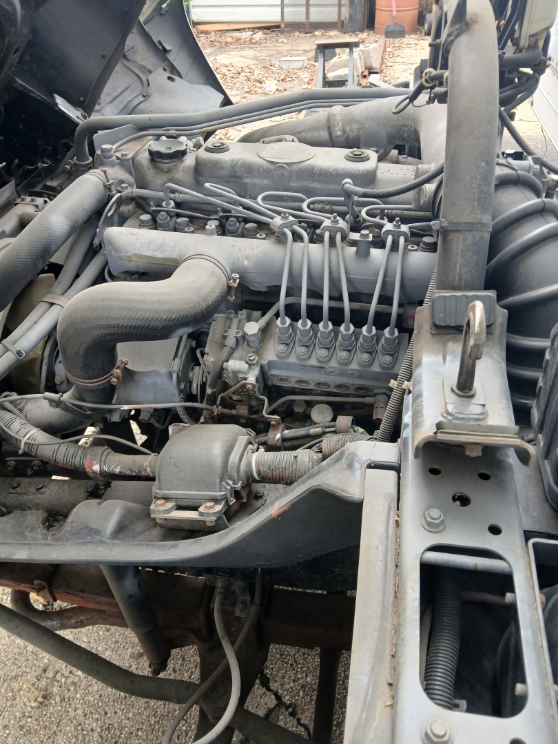 Truck engine bay with inline diesel engine showing intake manifold, fuel lines, and surrounding components.