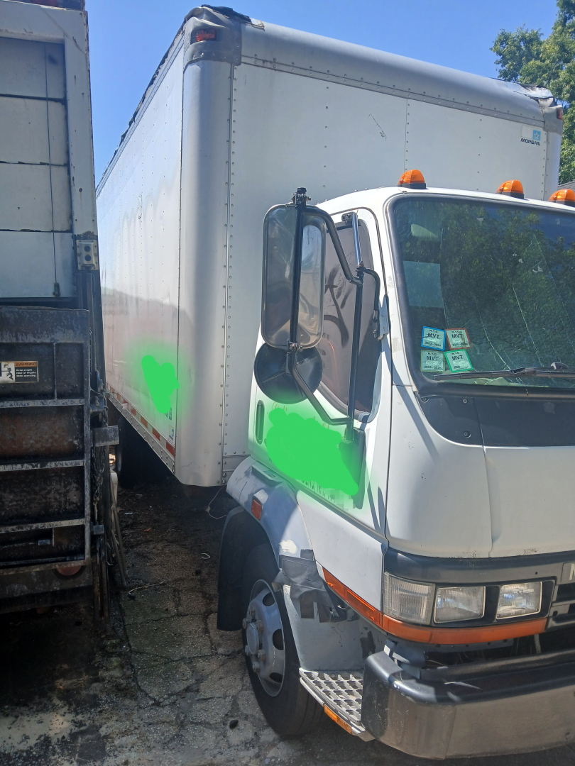 Truck cab with box truck body showing side view mirror and front grille; green highlight on door area; orange clearance lights on roof; side panel text not legible.