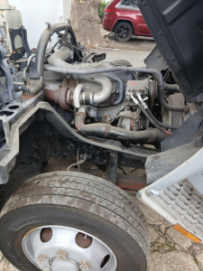 Engine bay view of a 2004 Mitsubishi FH truck showing turbocharger piping, hoses, and engine components near front wheel.