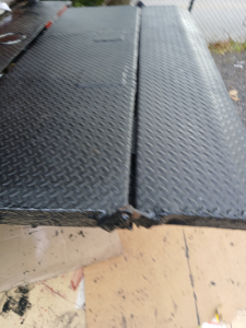 Diamond plate metal truck bed with seam in center and edge damage visible on the 2004 Mitsubishi FH truck bed area.