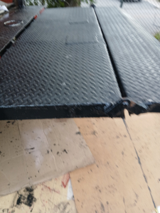 Truck bed or platform with diamond plate surface showing textured metal panels and edge seam.