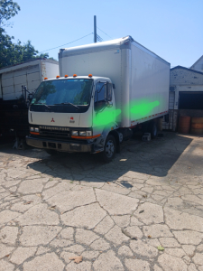 Mitsubishi FH box truck in a lot, front cab view with a large white cargo box attached.