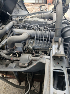 Truck engine bay with inline diesel engine showing intake manifold, fuel lines, and surrounding components.