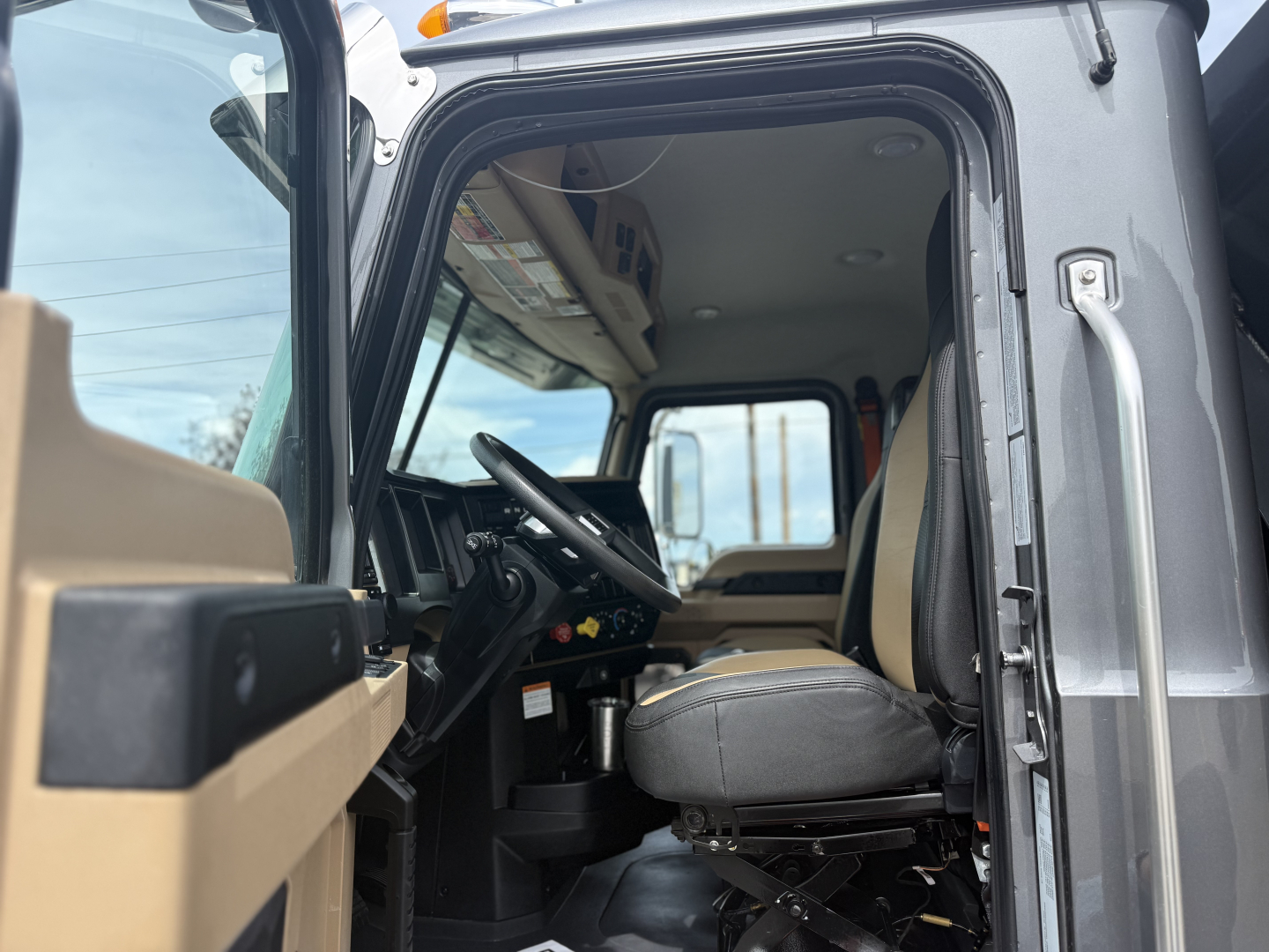 Truck cab interior of a Mack GR64F showing steering wheel, driver seat, and dashboard from the open door.