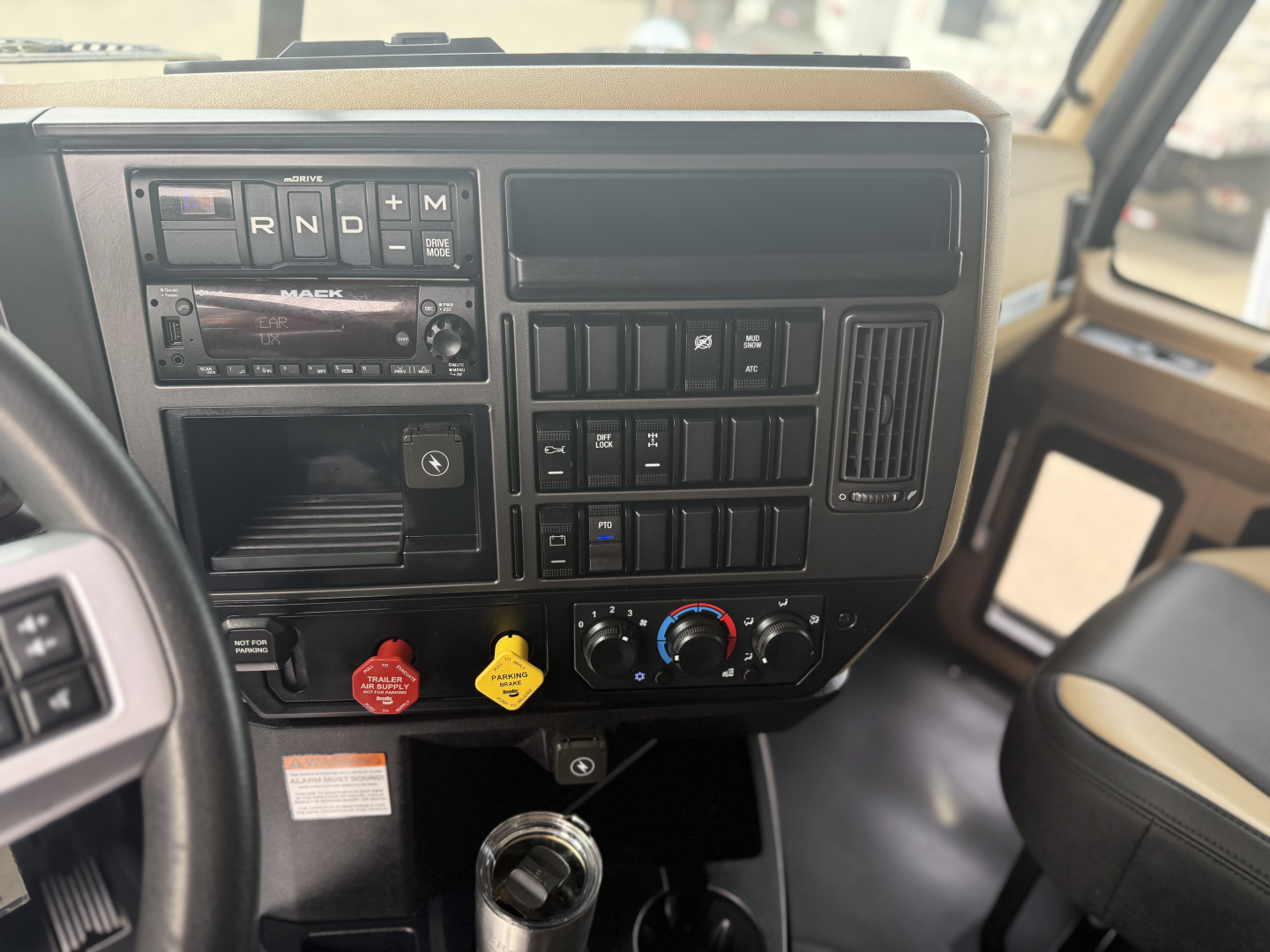 Mack GR64F dash showing gear selector R N D, control panel with climate dials, aux switches, and radio; steering wheel visible.